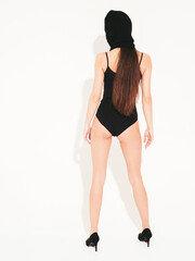 Beautiful sexy woman in black swimwear bathing suit. Model wearing bandit balaclava mask.Hot girl posing near white wall in studio.Seductive female in nice lingerie.Crime and violence