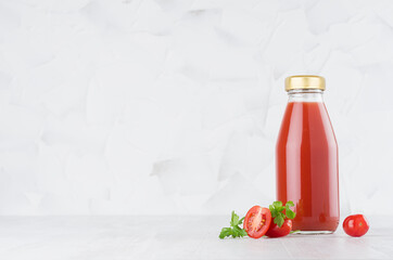 Fresh red tomato juice in glass bottle  template with green parsley, vegetables slices on wood table and white background with copy space.
