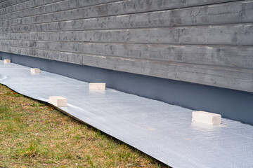 Tarpaulin on the ground next to building wall for painting plinth. Preparation before wall...