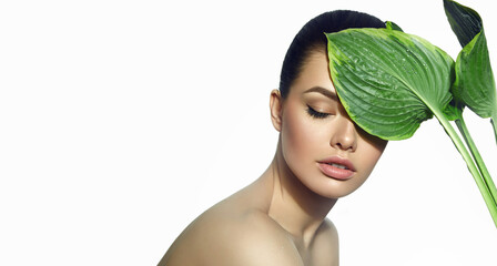A beautiful tanned green-eyed girl with natural make-up keeps wet exotic leaves on her face.