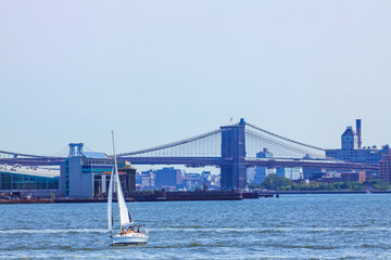 A sail boat in New York, with Brooklyn Bridge in the back.