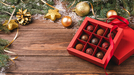 Chocolate candies in a red craft box wooden Christmas background fir branches of a New Year's toy. Flat layout top view.