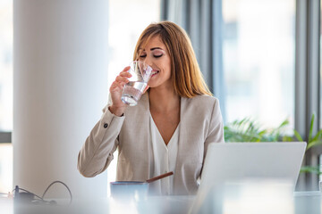 Businesswoman drinking a glass of water at her desk in the office. Young woman working in her...
