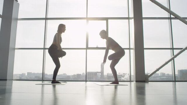 Back light long shot footage of two sporty women standing in front of each other doing balancing yoga exercise