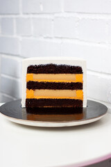 Slice of layered cake with chocolate sponge layers and orange filling on white background.