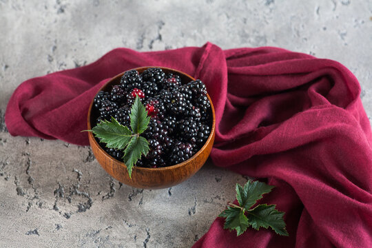 Sweet blackberry and leaves in wooden bowl on grey stone background. Top view.