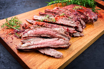 Traditionelles gegrilltes dry aged Wagyu Flank Steak aufgeschnitten und angeboten Kräuter und Chili Pulver als close-up auf Modern Design Holz Board