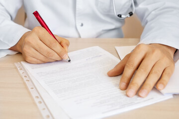 doctor's hands in white coat signs documents at the table with red pen close-up