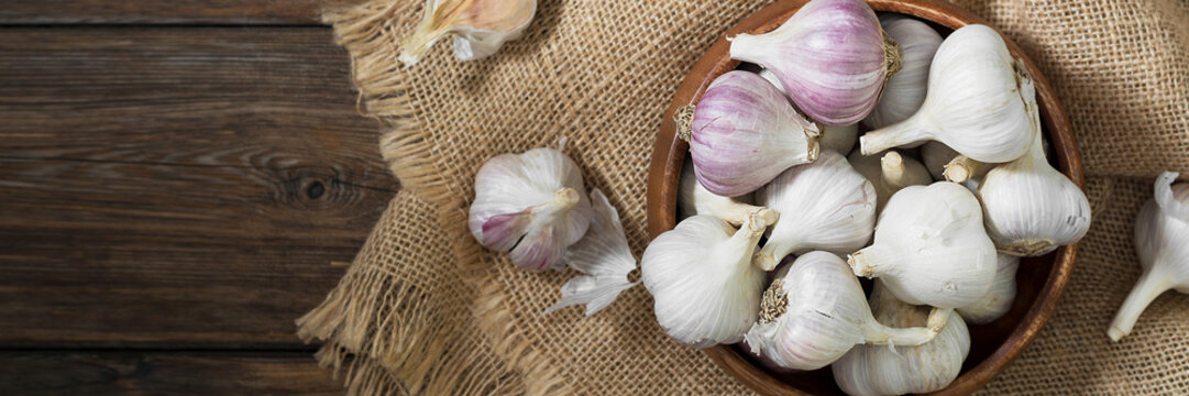 Garlic in a wooden bowl on a wooden table. lots of garlic in a bowl. Garlic close-up. Banner with space for text