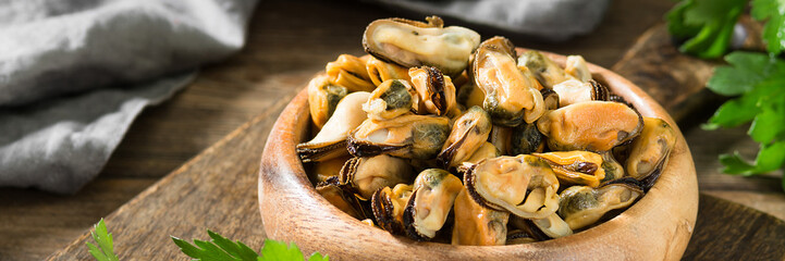 Mussel meat in a wooden bowl on a brown wooden kitchen table. A lot of mussels in the plate. Rustic style. Banner with space for text