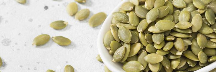 Pumpkin seeds in a white bowl on the light gray kitchen table. Lots of pumpkin seeds in a bowl close-up. Banner with space for text