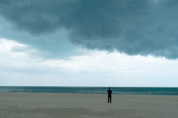 Fototapeta na wymiar Man standing in beach with dark huge cloud sky black stormy cloud motion in big rain day.
