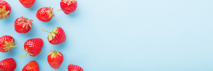 Red bright strawberries on light blue table background. Wide banner of beautiful fresh berries. Pastel color. Closeup. Flat lay. Empty place for text. Top down view.