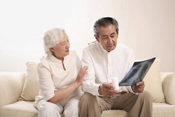 Senior man with a bottle of pills looking at his x-ray sadly, senior woman consoling him