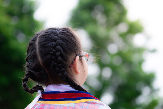 Asian Little Child Girl With Black Hair Braid Turned Her Back To The Camera. Children Wear School Uniforms And Wear Glasses. Kid 6 Years Old.