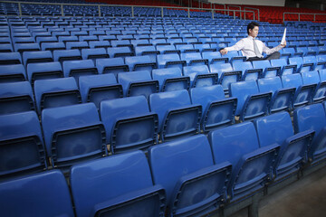 Businessman reading a newspaper in an empty stadium