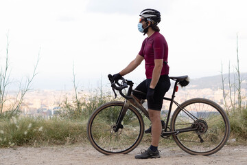 
Male cyclist with a gravel bike observing the landscape with a medical mask. Concept: sport and coronavirus