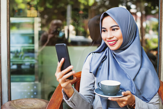 Pretty Indonesian woman drinking coffee and talking on video call