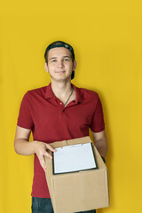 Delivery young man in burgundy t-shirt with black cap standing on a yellow background, smiling to camera. Your shipping is here.