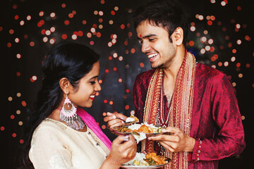 Obraz na płótnie Canvas Beautiful Indian couple eating food over festive bokeh background