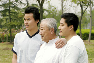 An old man standing between his two sons in the park