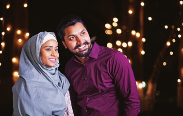 Beautiful cute muslim couple standing in decorated garden on Eid al-Fitr / Eid al-Adha / Ramadan night