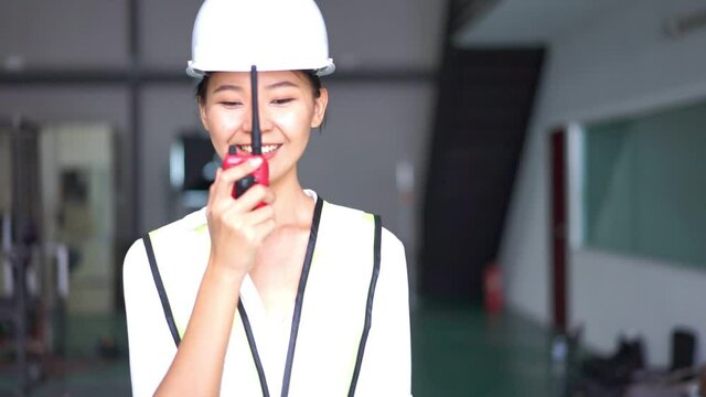 Female engineer wear yellow uniform use radio to communicate with team in factory.