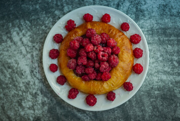 cheesecake with fresh raspberries on a white plate; dark background shot from above
