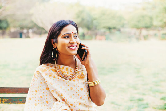Beautiful indian woman in saree talking on mobile phone, sitting in the park