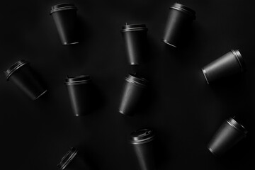 Scattered black paper cups close up on a black background. Recycling craft paper cups of coffee to go. Selective focus. Craft cup for hot beverage, takeaway. Disposable cup. Minimalist Style