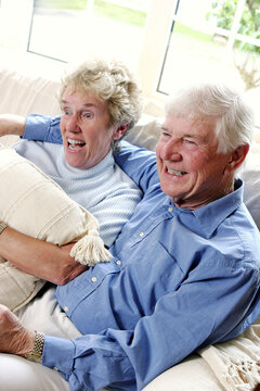 An Old Man Sitting On The Couch With His Arm Around His Wife