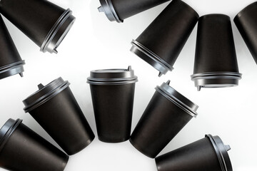 Pattern of black paper cups for tea or coffee on a white background. Recycling craft paper cups of coffee to go. Selective focus. Craft cup for hot beverage, takeaway. Disposable cup. Minimalist Style