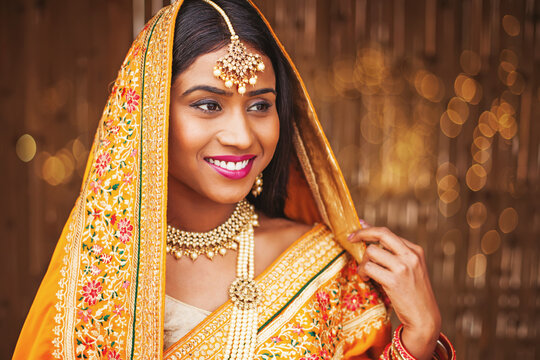 Beautiful young Indian woman dressed as a bride, wearing maang tikka and necklace with perl mala, her head covered with saree pallu