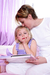A woman sitting on the bed kissing her daughter's head