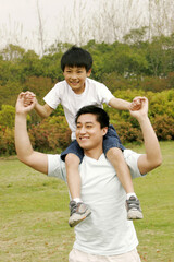 A man giving his son a piggy back ride in the park