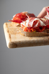 Wooden try with toasted brad slice with fresh tomatoes and cured ham. Delicious appetiser Italian...