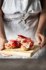 Obraz na płótnie Canvas Woman holding wooden try with toasted bread slice with fresh tomatoes and cured ham. Delicious appetiser Italian prosciutto and Spanish Iberian ham snack
