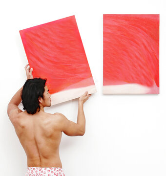 Back Shot Of A Shirtless Guy In Boxer Shorts Hanging Up Paintings On The Wall