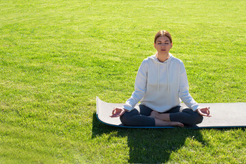 A woman practices yoga outdoors on the grass. Copy space