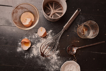 Fototapeta na wymiar Scarlet egg, whisk and flour on a black wooden table. Making cupcakes at home.