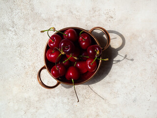 brass bowl with cherries berries on beige background, top view. daylight, summer concept