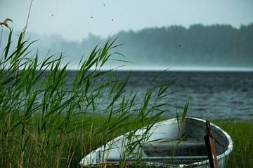 Moody rain landscape with boat on the lake and mist. View on lake boat while raining. Rainy seascape on the lake.