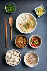 Rice stick noodles with fish ball in white bowl. Garlic cracklings with lard, mined pork, pickled chili, lime and coriander with spring onion various ingredients and condiment on table.