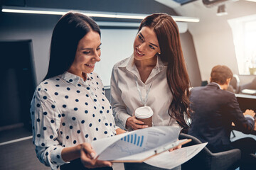 Businesswomen talking in busy meeting area of large modern office