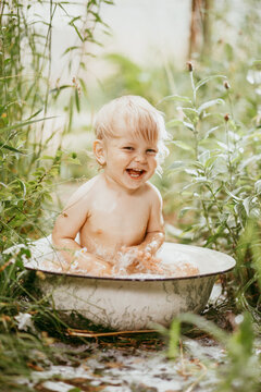 Cute funny little boy bathing in galvanized tub outdoor in green garden