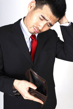 Businessman scratching his head while looking at his empty wallet