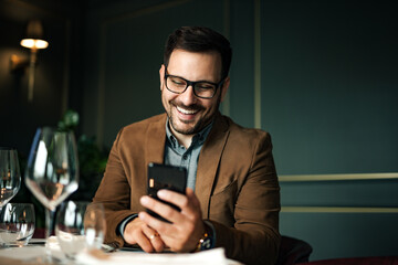 Cheerful man using smart phone in fancy restaurant, portrait, close-up.