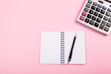 Large silver calculator with black pen and white paper notebook laying on a pink background. Concept of finance, business, calculations, education, school, math, accounting, computing, profit, tax