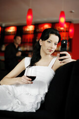 Woman text messaging on the mobile phone while holding a glass of wine