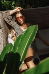 Close up outdoor fashion portrait of young woman with perfect bronze tanned skin, laying and...